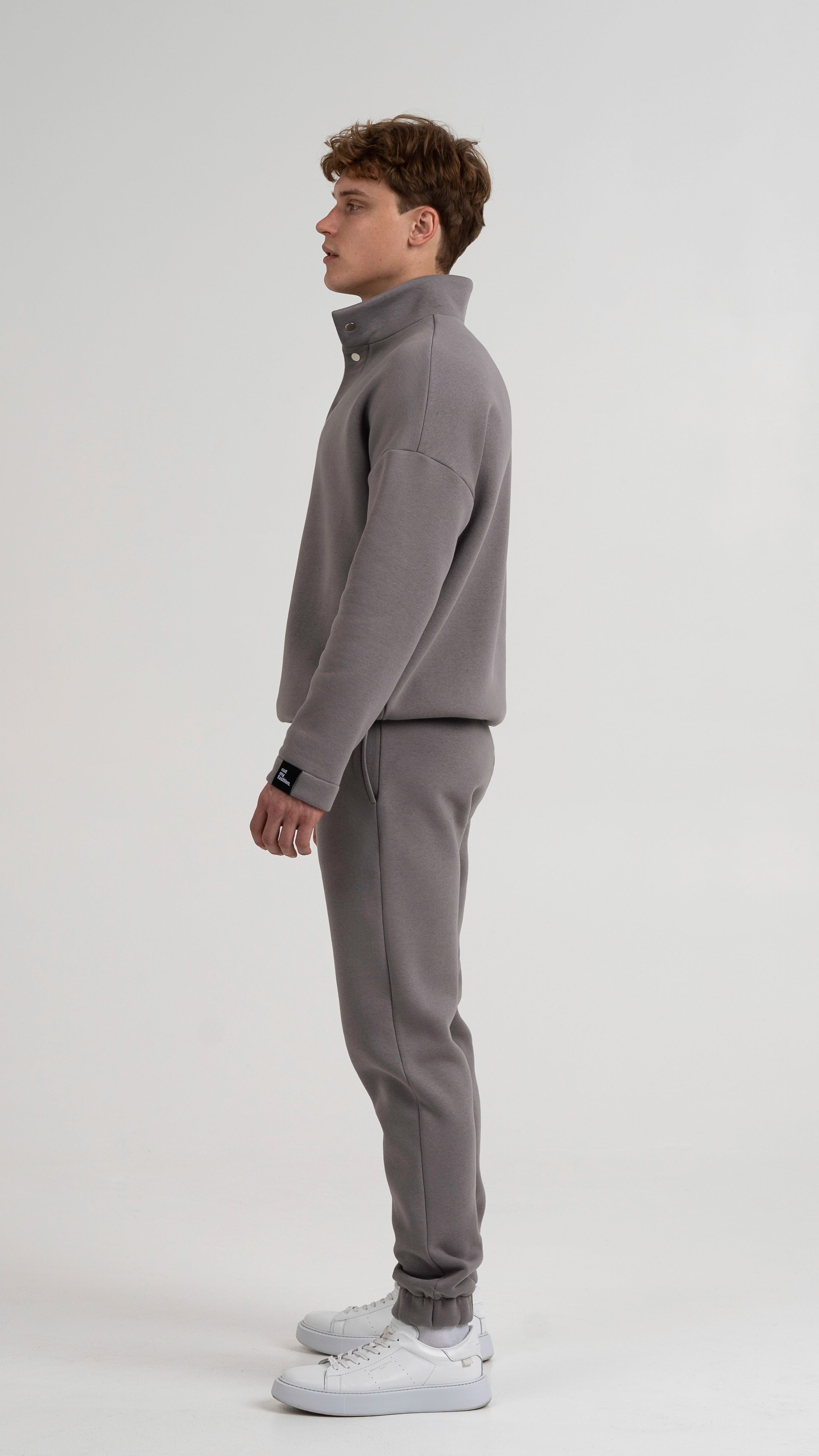 Vyriškas modelis pozuoja, dėvėdamas Cutmyfashion pilkos spalvos laisvalaikio treningus, demonstruojant treningo šoną