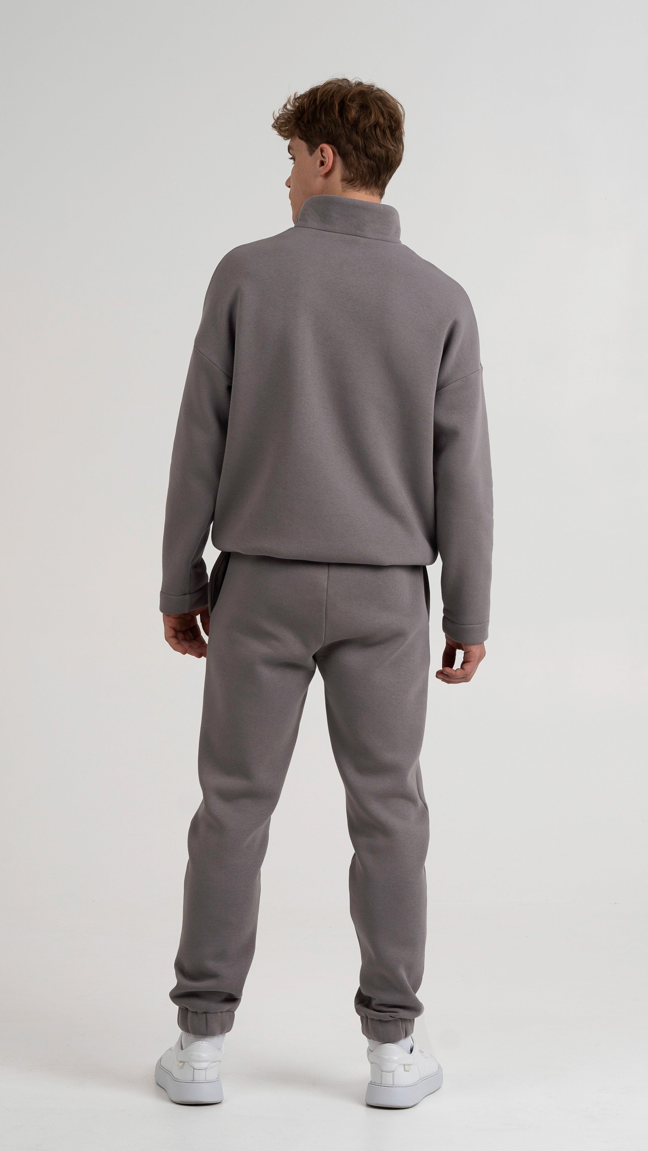 Vyriškas modelis pozuoja, dėvėdamas Cutmyfashion pilkos spalvos laisvalaikio treningus, demonstruojant treningo nugarą