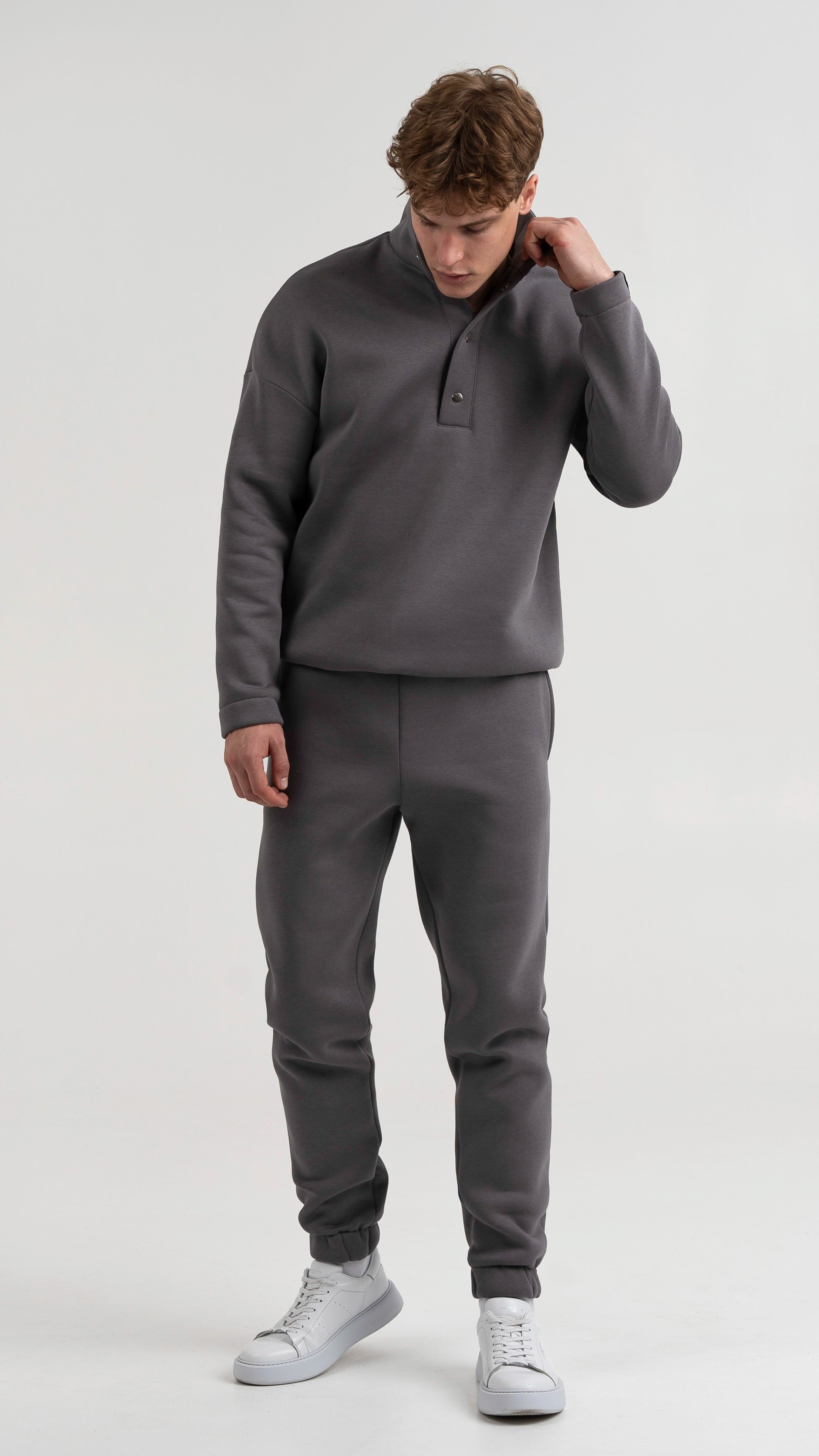 Vyras pilkuose cutmyfashion treninguose, stovintis profiliu ir žvelgiantis į šoną