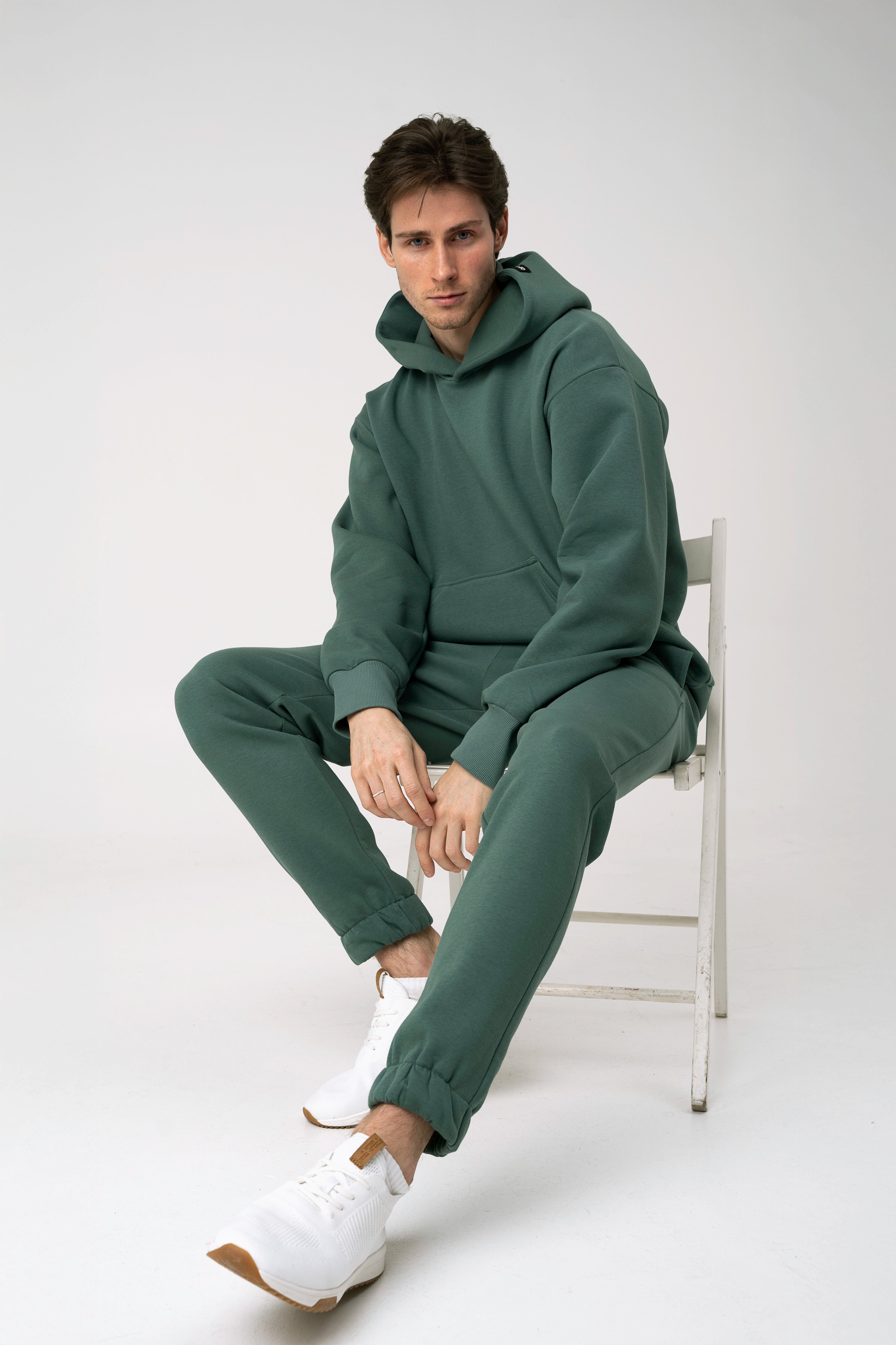 Vyras sėdi ant kėdės baltame fone ir dėvi CMF By Kamilės laisvalaikio treningus CMF184