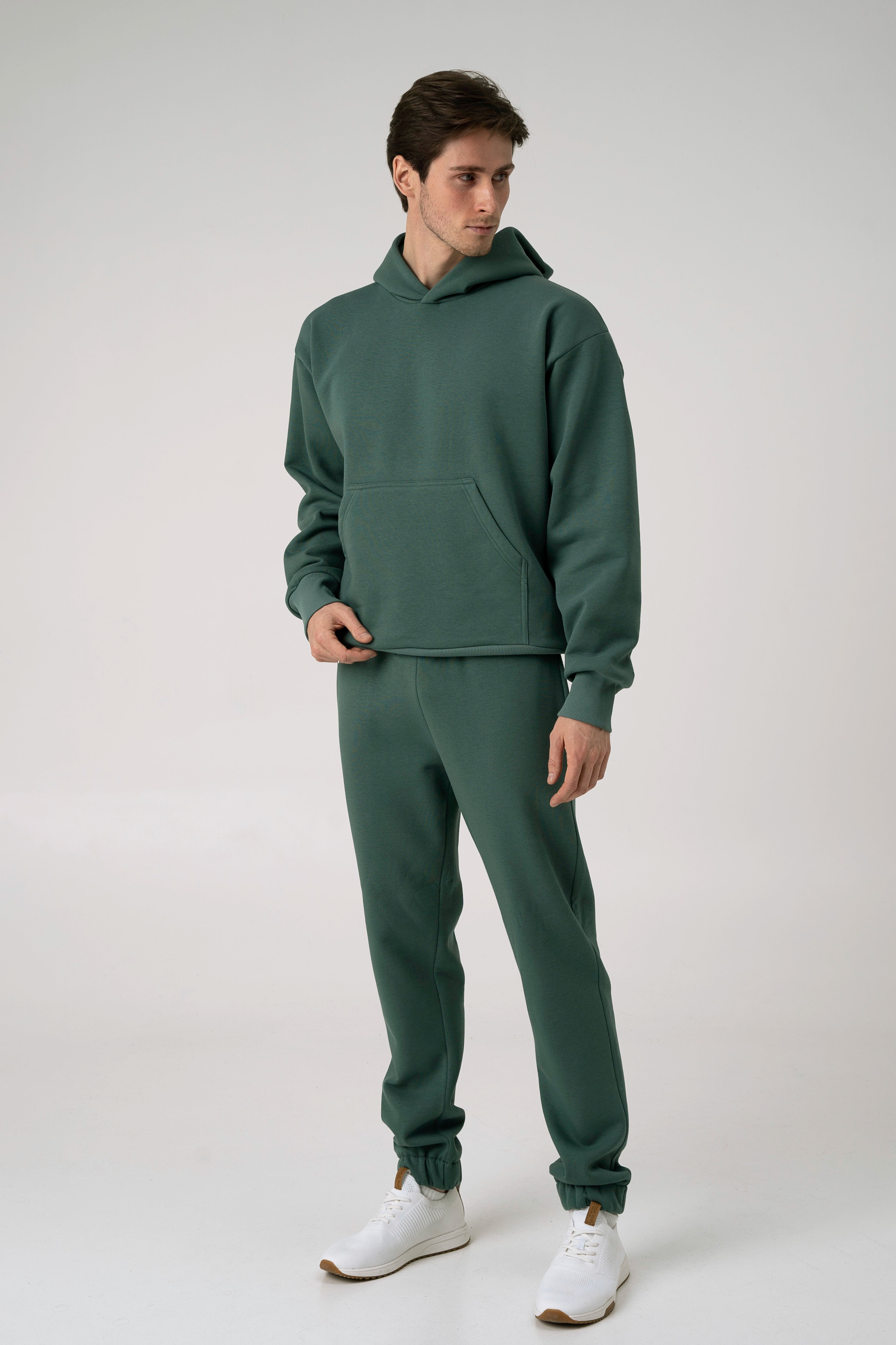 Vyras stovi pasisukęs šonu baltame fone ir dėvi CMF By Kamilės laisvalaikio treningus CMF184