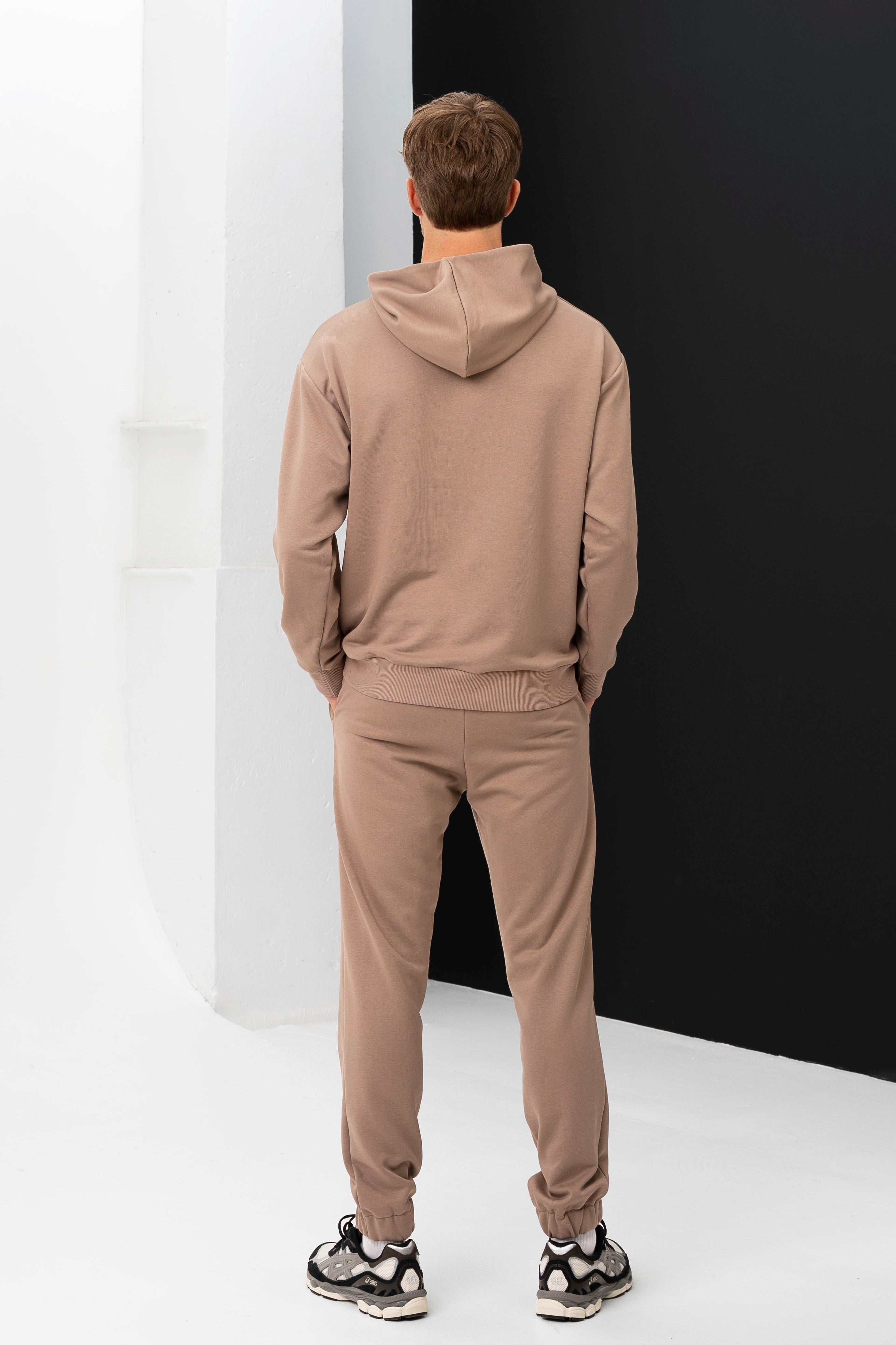 Modelis atsuktas nugara, demonstruoja smėlio spalvos vyriškų treningų nugaros dalį