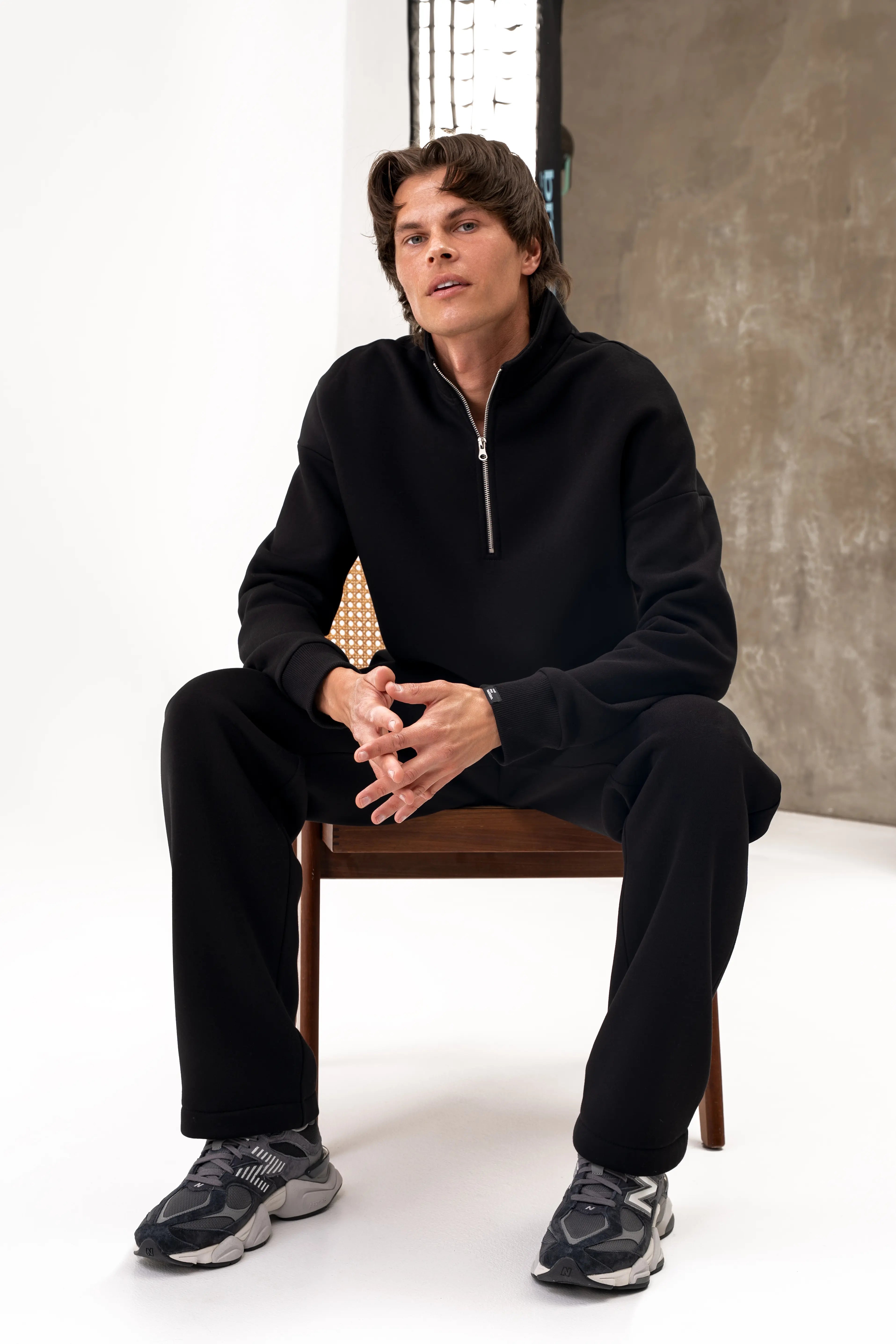 Men's black "Vilius" leisure tracksuit while seated – a jumper with a half zip and trousers with pockets