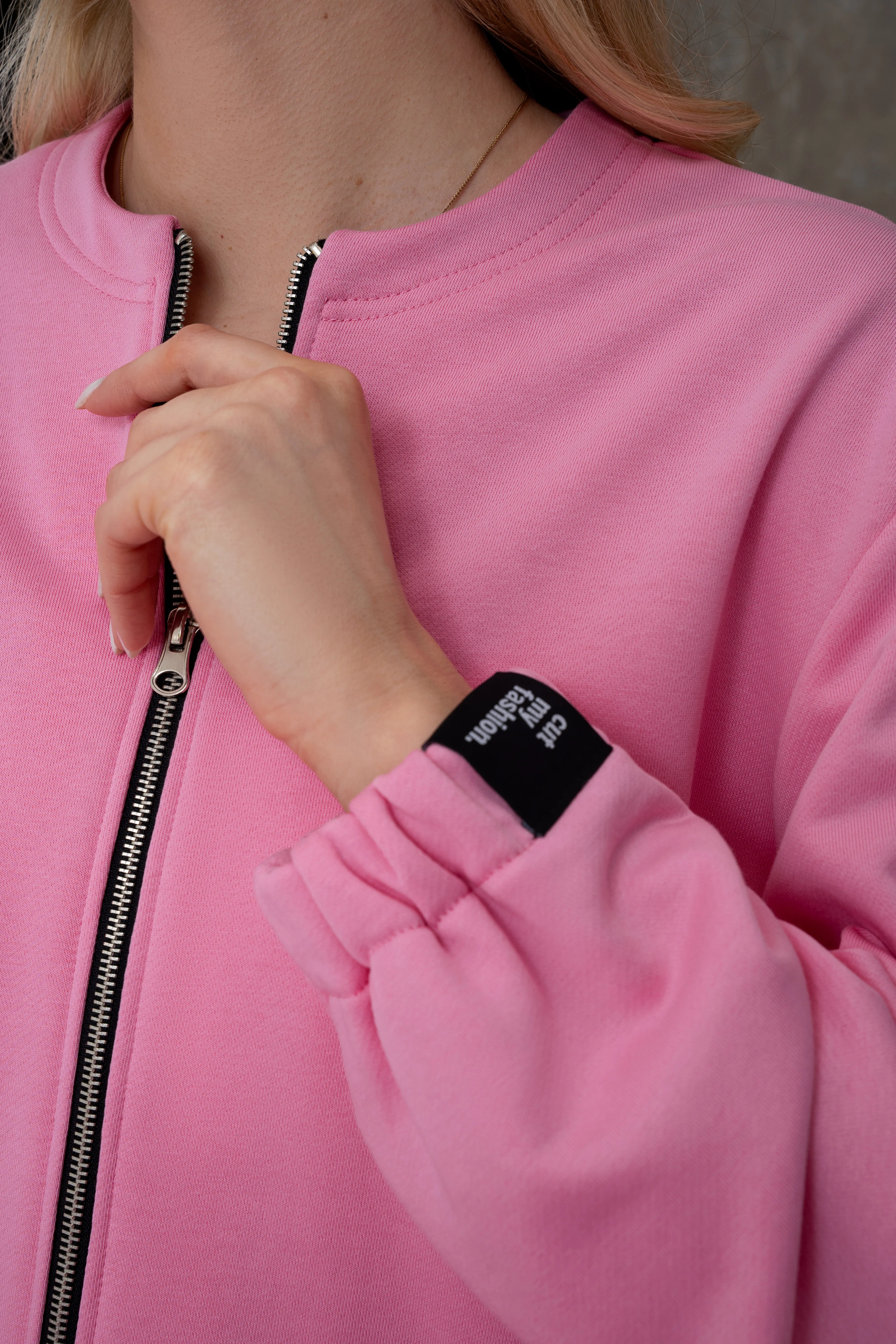 Pink women’s loungewear sweatshirt with a full-length metal zip, an elastic gathered cuff, and a black cutmyfashion label, detail view