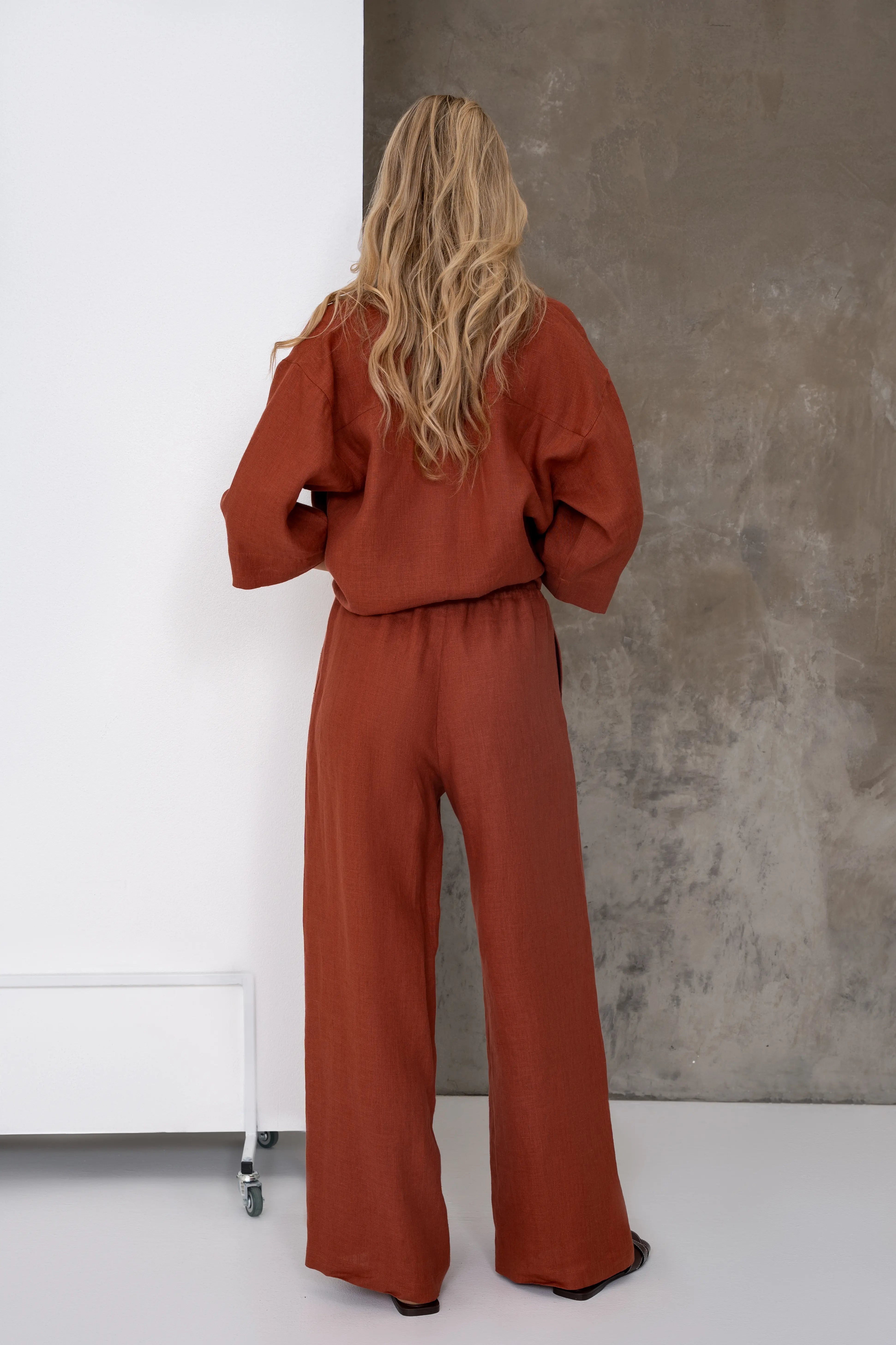 Brick-colored linen women's trousers with an elastic waistband and wide legs, full-length back view