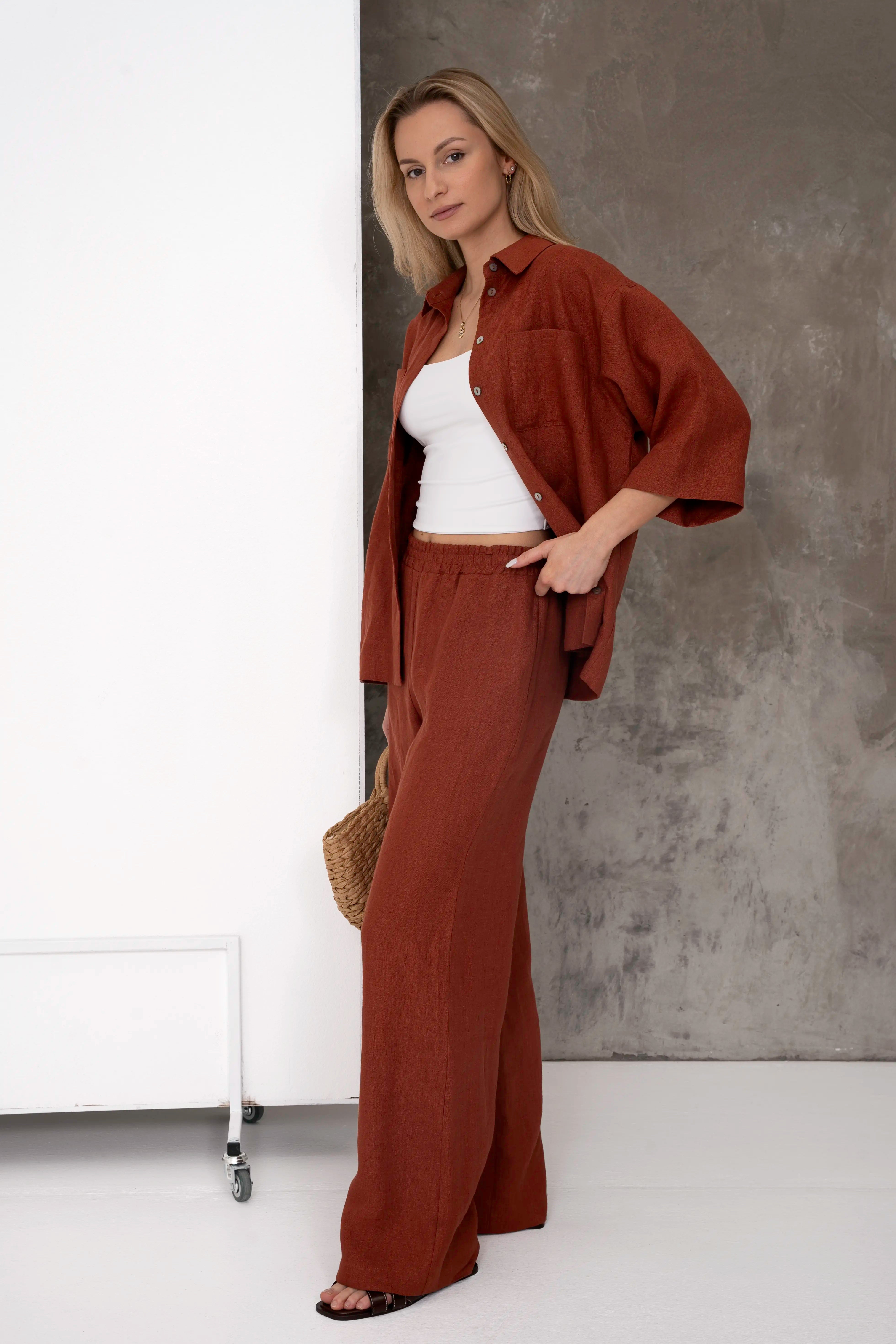 Brick-coloured linen women’s trousers, straight silhouette, paired with an open shirt from the side