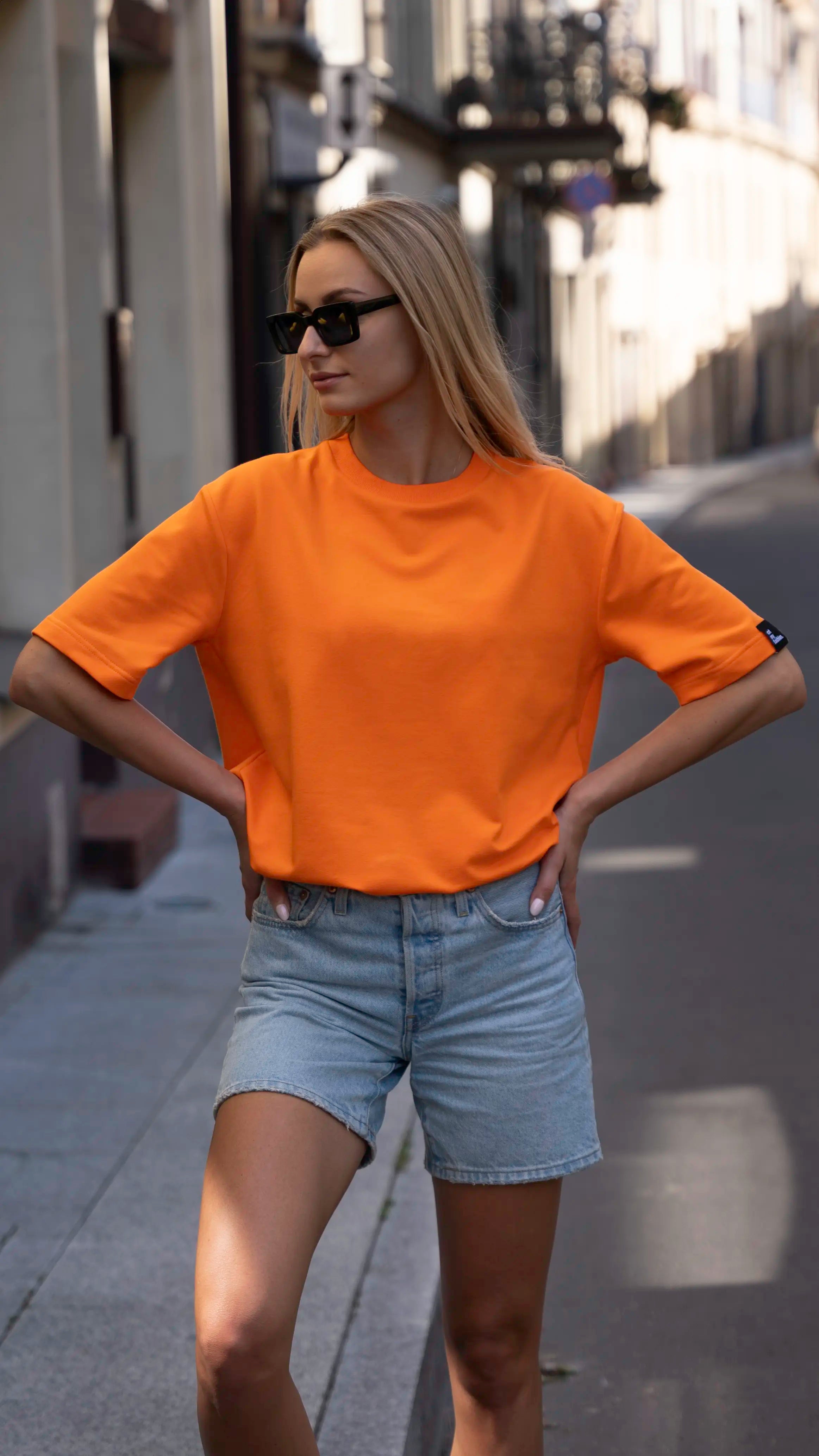 Mergina mieste dėvi oranžinius oversized stiliaus cutmyfashion moteriškus marškinėlius
