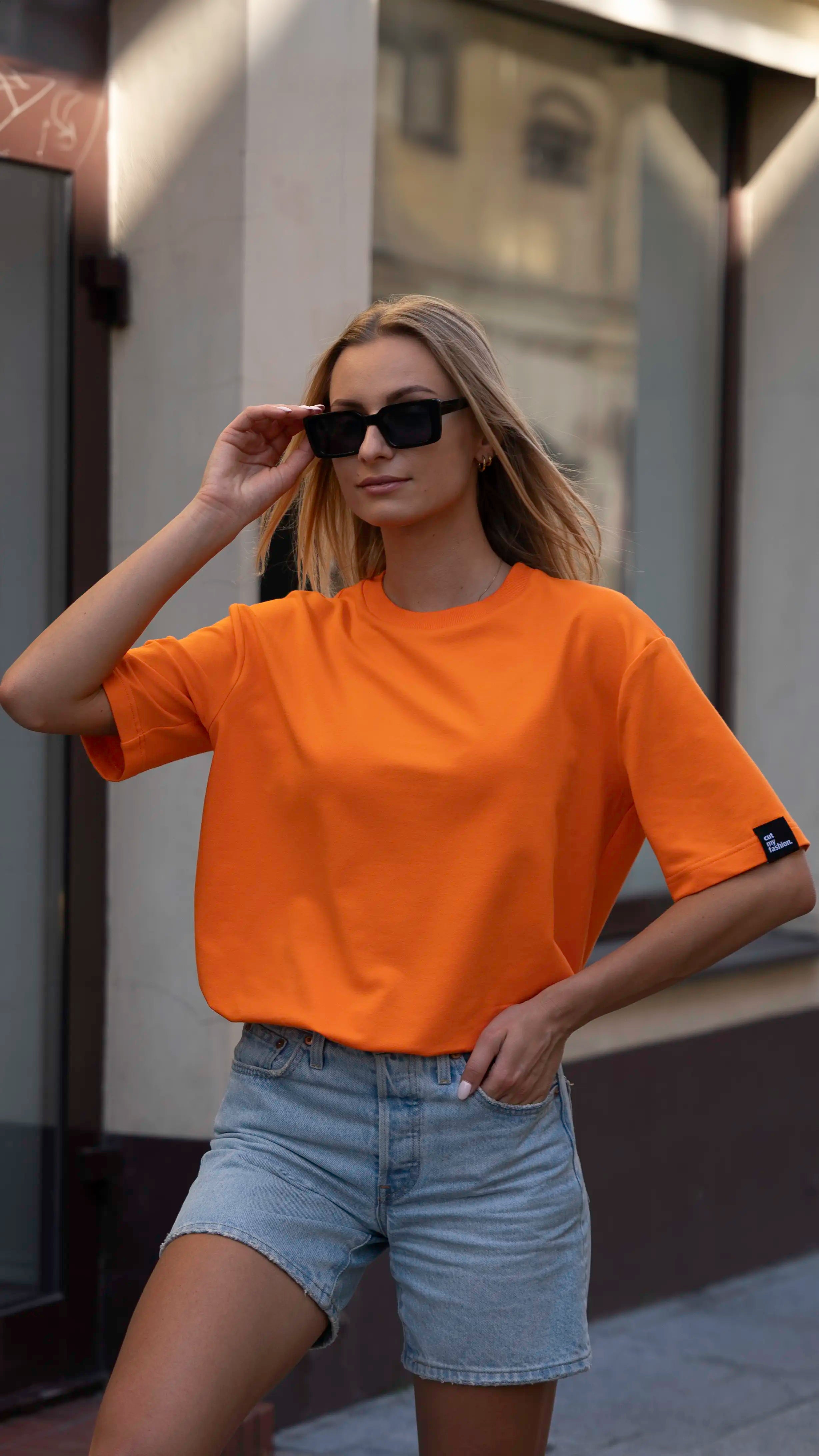 Mergina mieste dėvi oranžinius oversized stiliaus cutmyfashion moteriškus marškinėlius