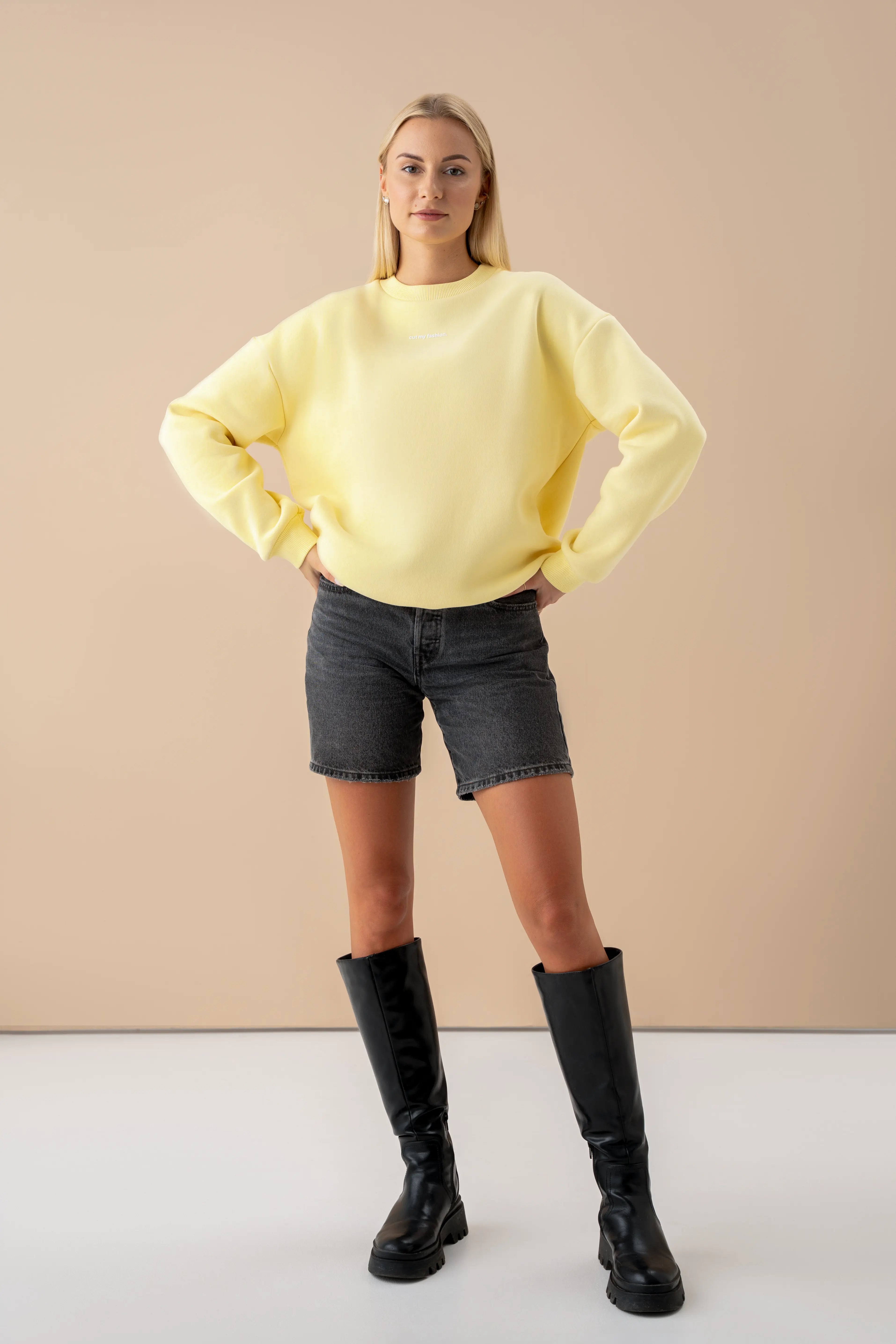 modelis vilki oversized geltoną cutmyfashion džemperį iš OEKO TEX medvilnės su pūkeliu, derina prie juodų šortų ir aulinukų studijos fone pagaminta Lietuvoje