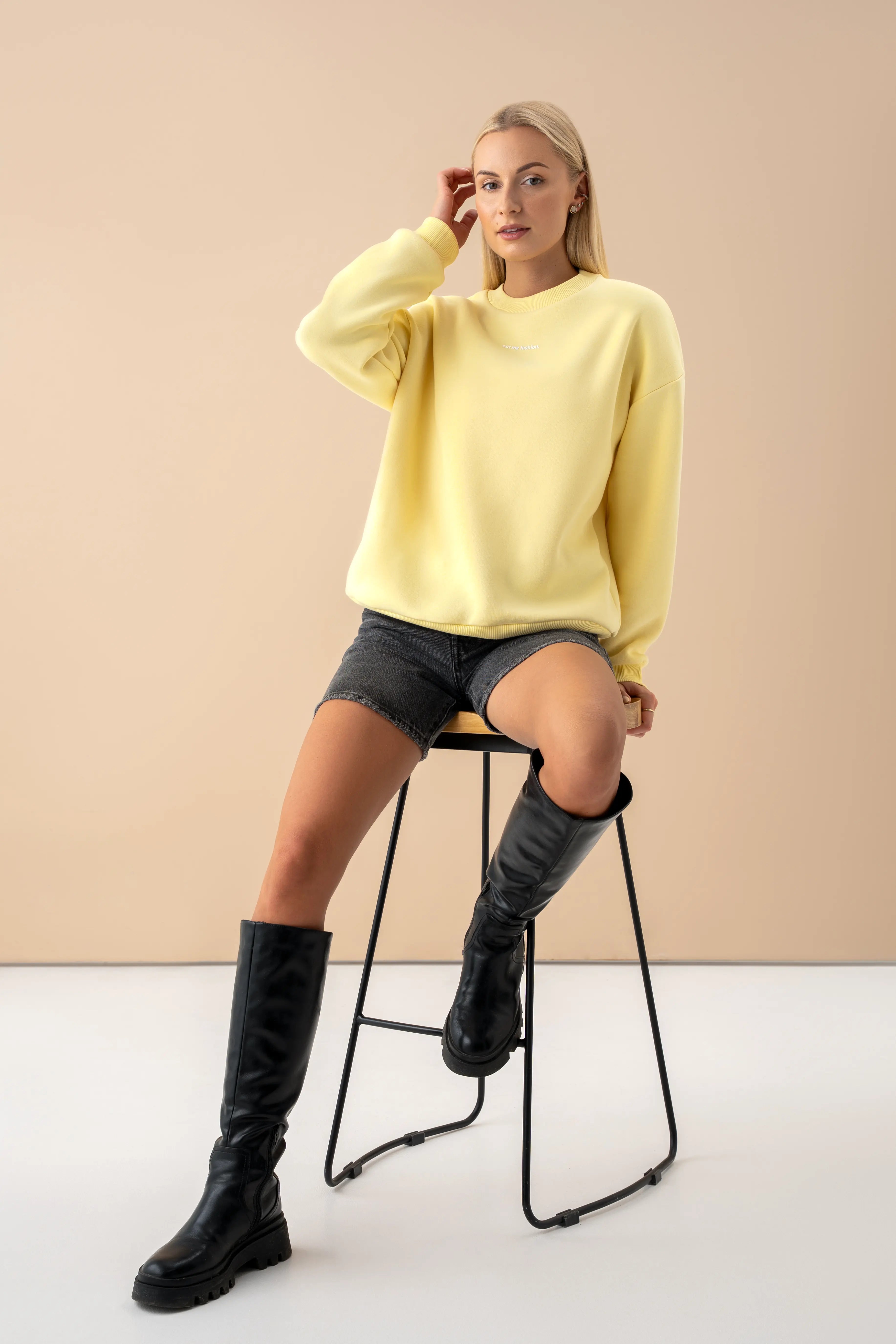 geltonas oversized cutmyfashion džemperis iš OEKO TEX medvilnės su pūkeliu modelis sėdi ant kėdės vilki juodus šortus studijos aplinkoje