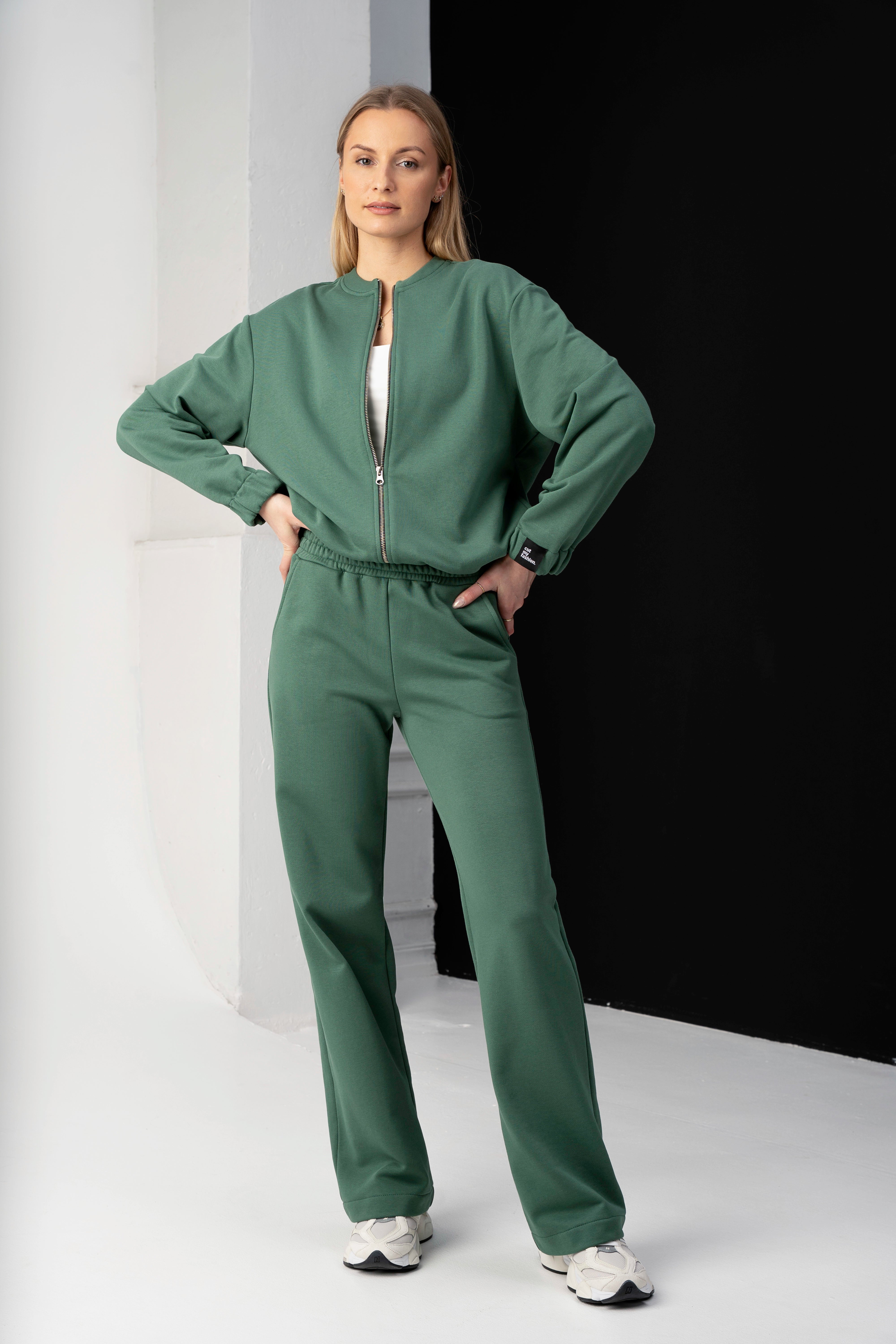 moteris vilki žalius cutmyfashion laisvalaikio treningus mėja, pozuoja studijoje, rankas laikydama ant klubų