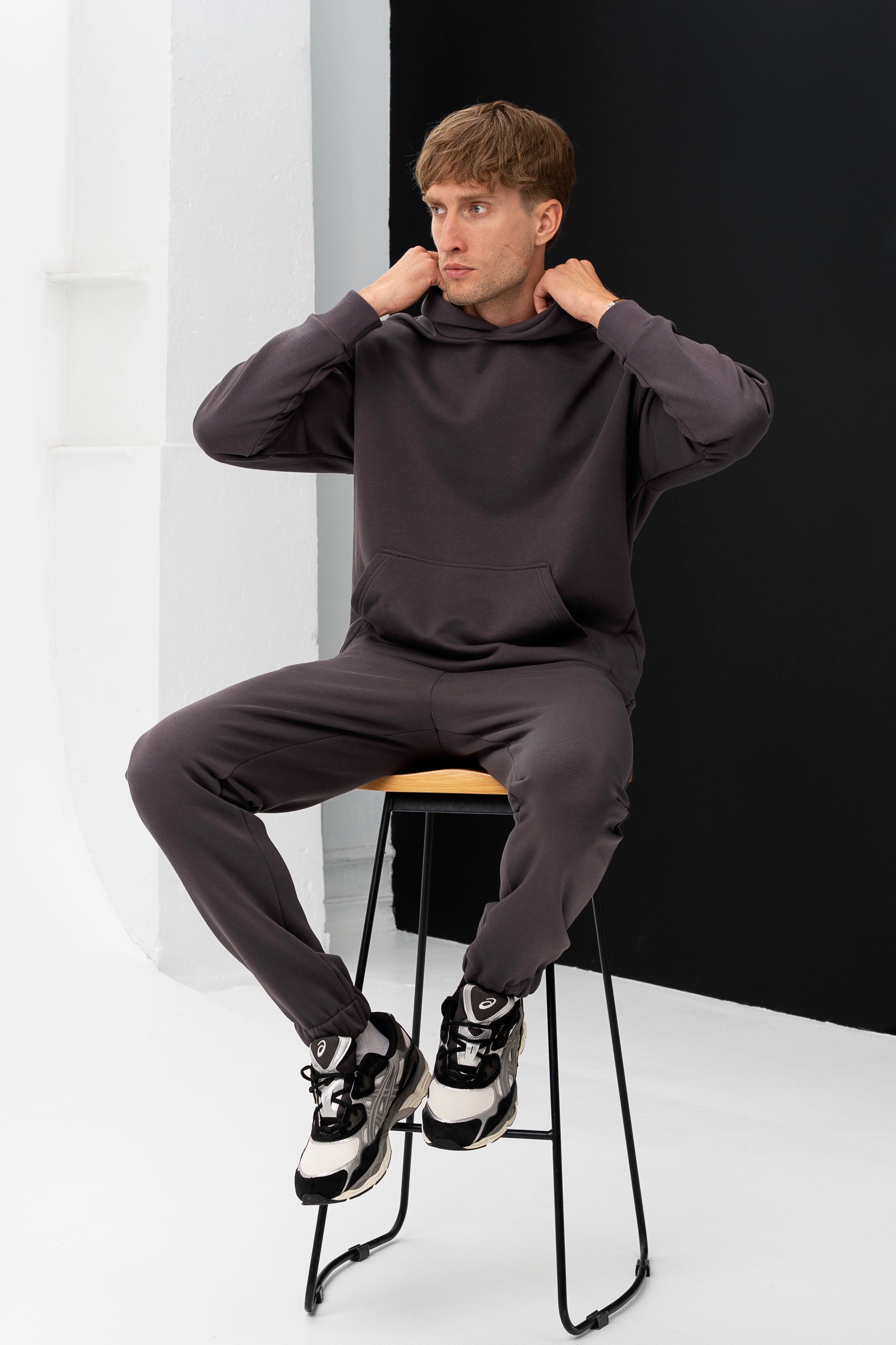 cutmyfashion vyras sėdi ant kėdės vilkėdamas tamsiai pilkus treningus – OEKO-TEX® sertifikuotas audinys, pagaminta Lietuvoje
