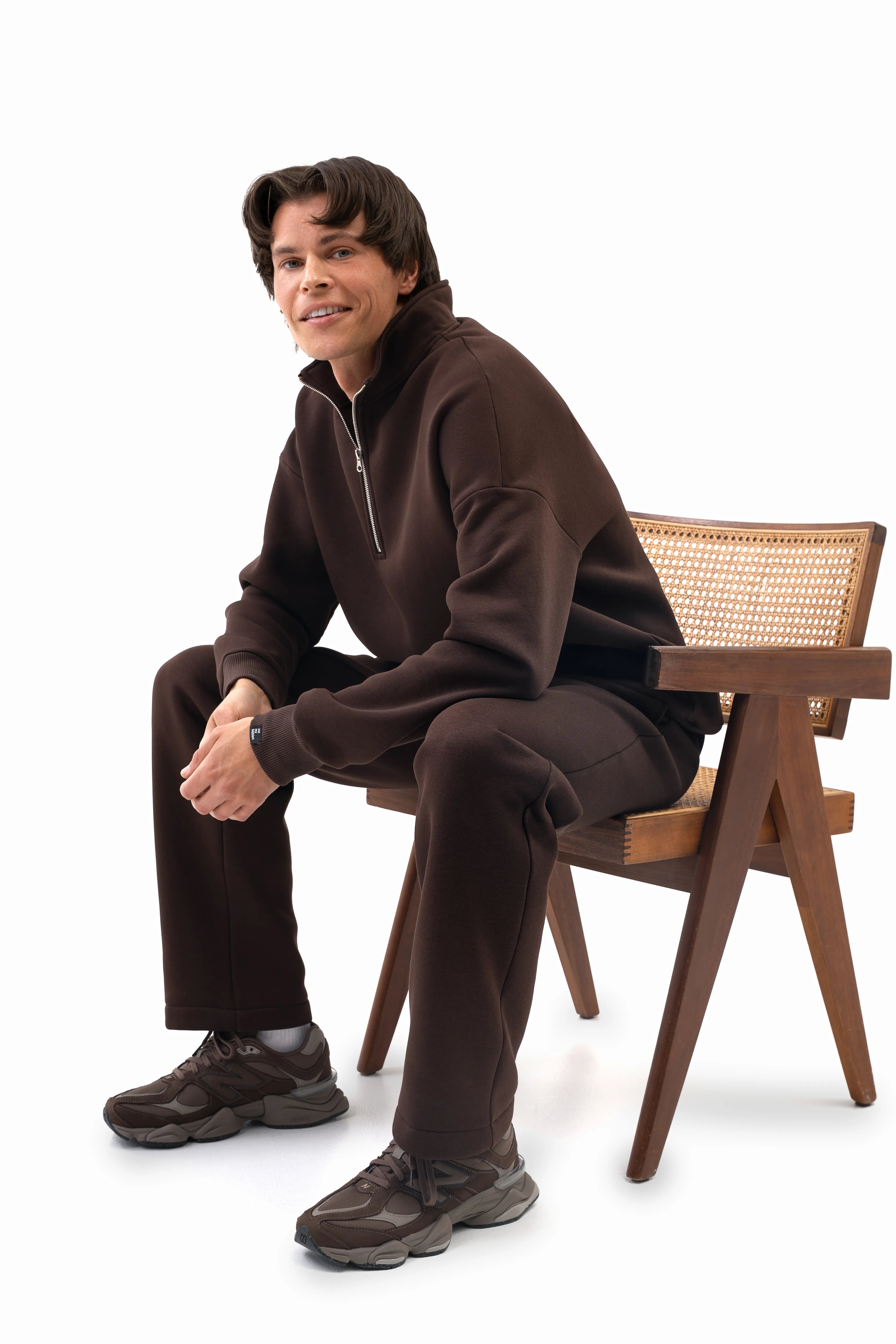 Vyriškas rudas laisvalaikio kostiumėlis su tiesiomis kelnėmis ir trumpu užtrauktuku, modelis sėdi ant kėdės