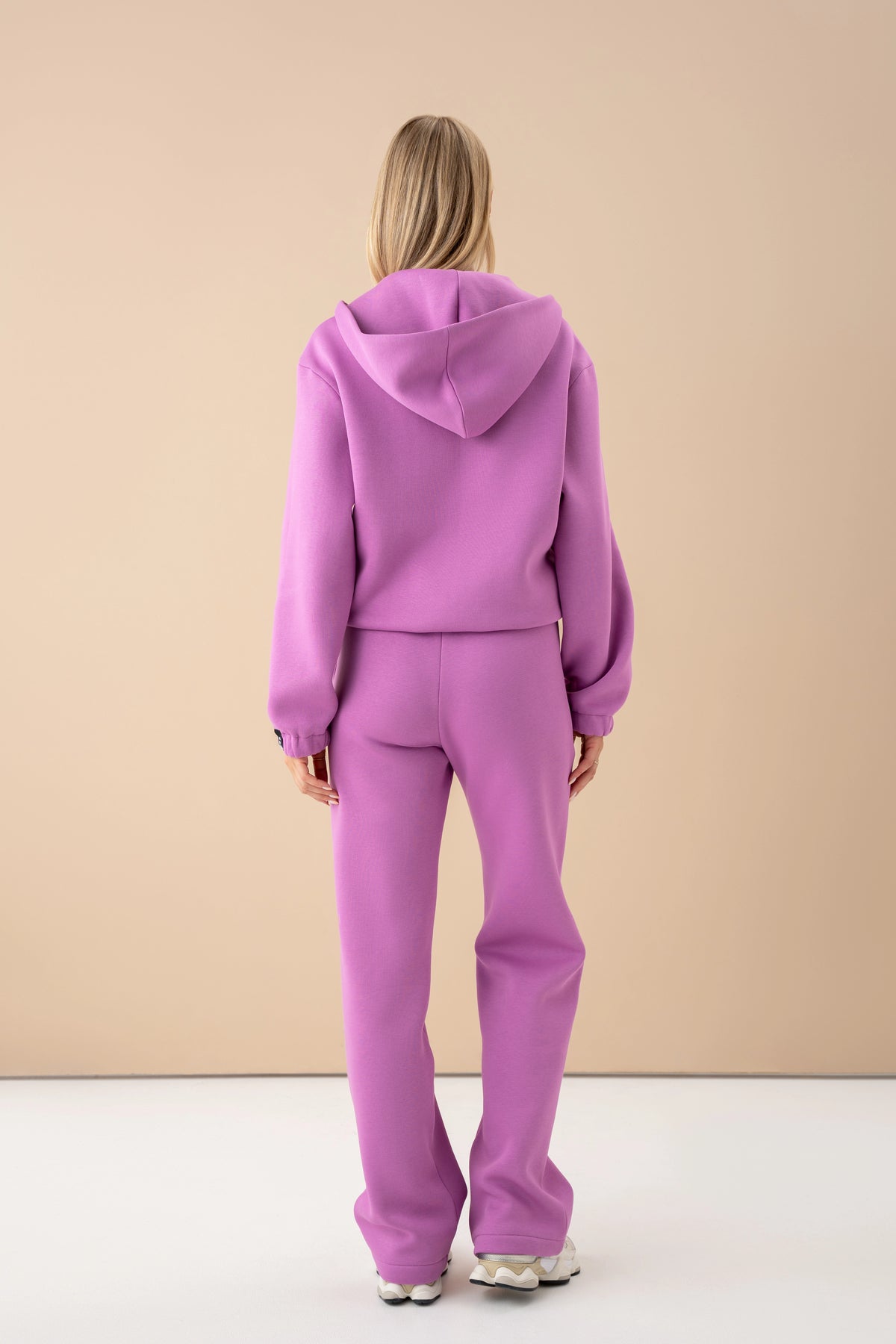 The model in a pastel pink sweater and trousers is turned with her back to the camera, wearing cutmyfashion in the studio