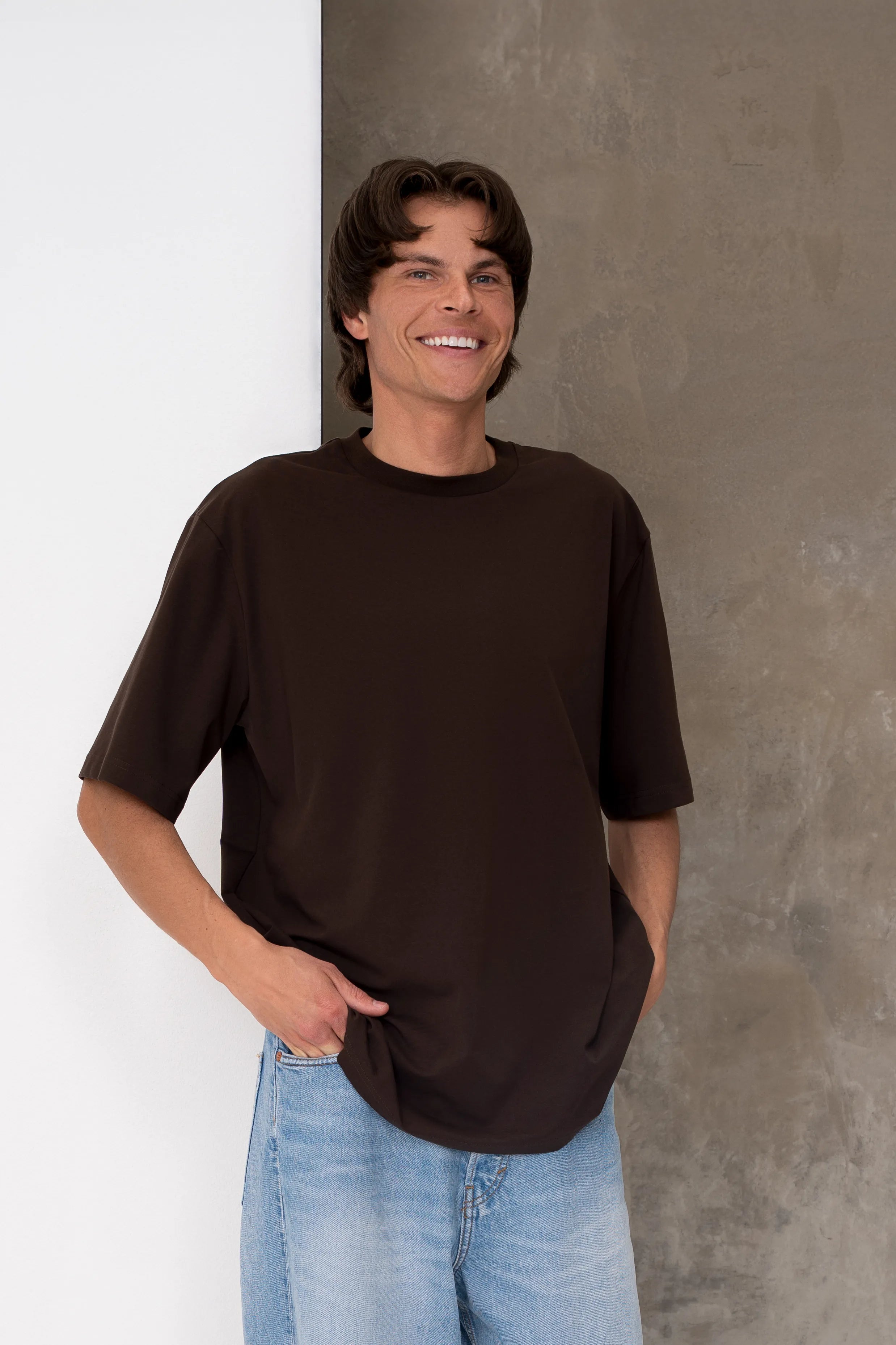 Rudi vyriški oversized marškinėliai trumpomis rankovėmis su nuleista pečių linija ir laisvu siluetu, derinami su šviesiais džinsais, pilnas vaizdas iš priekio